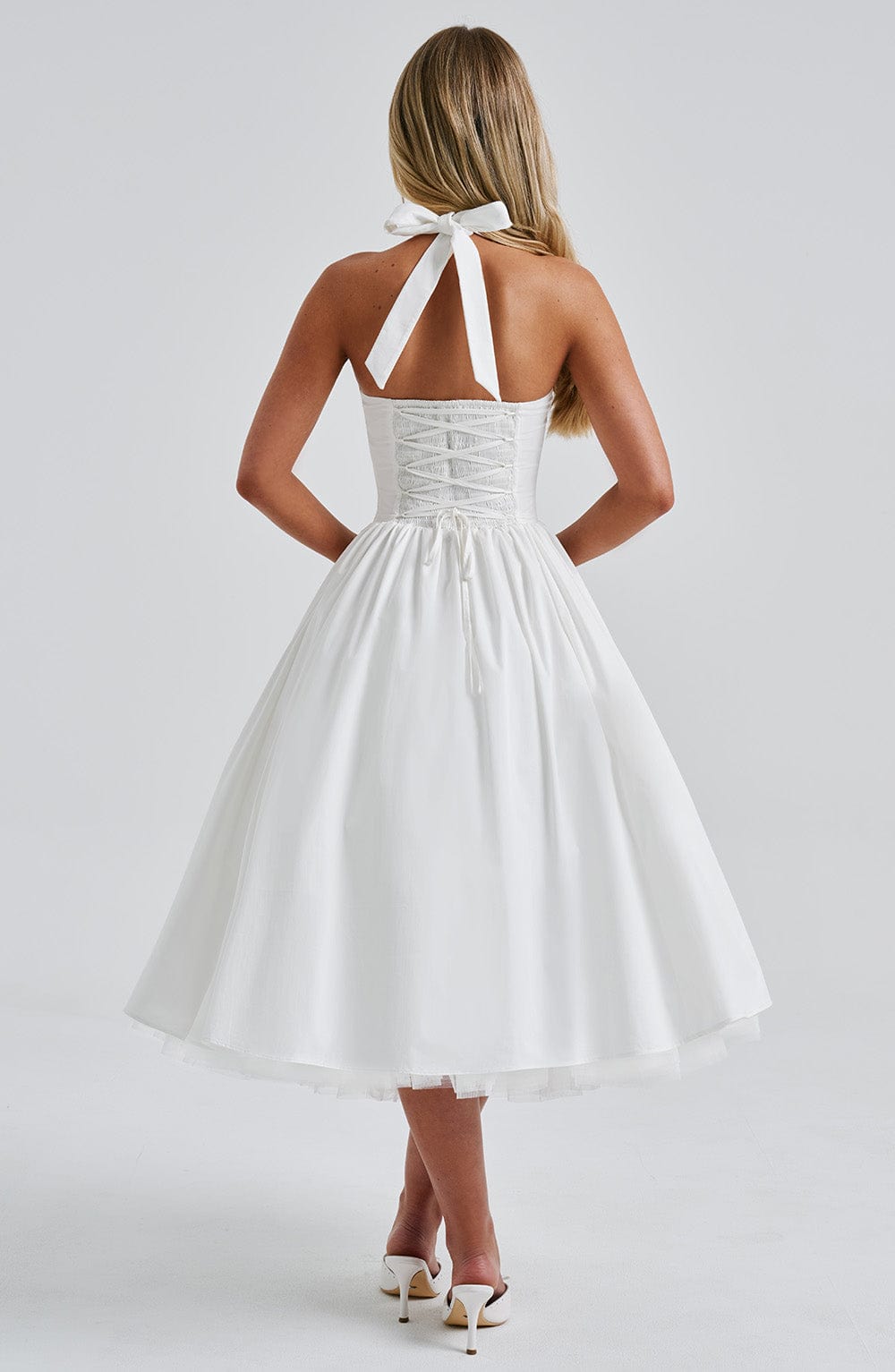 Back view of the white halter midi dress, showing the lace-up corset detail and tied halter straps.