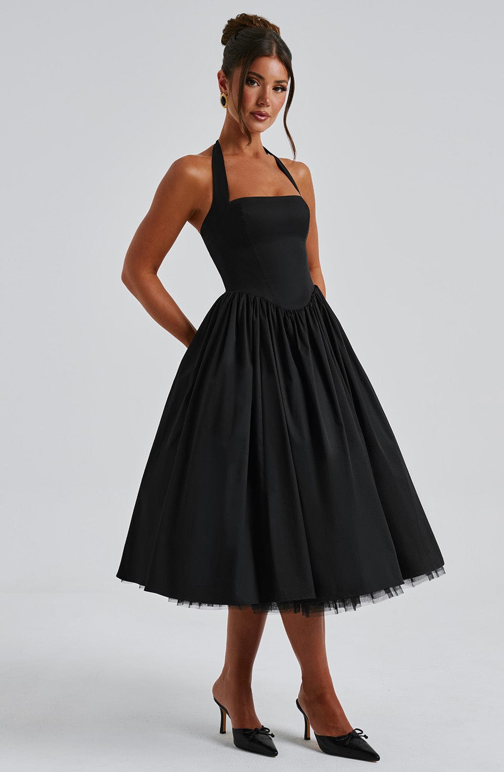 Side view of the black halter midi dress, showcasing the gathered waist and the mid-calf length of the skirt.