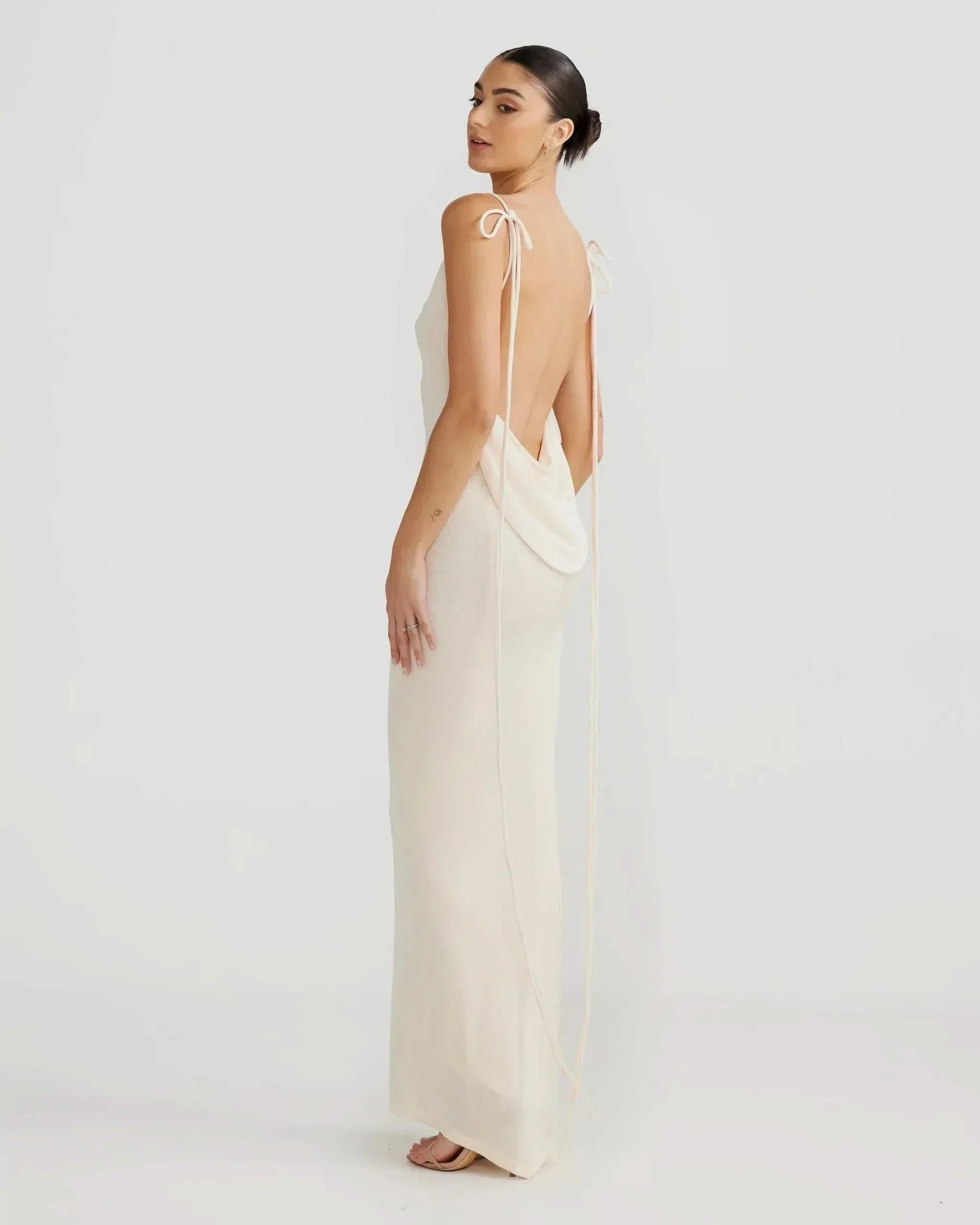 Side profile of a model wearing off-white backless cowl neck maxi dress with long tie straps for women