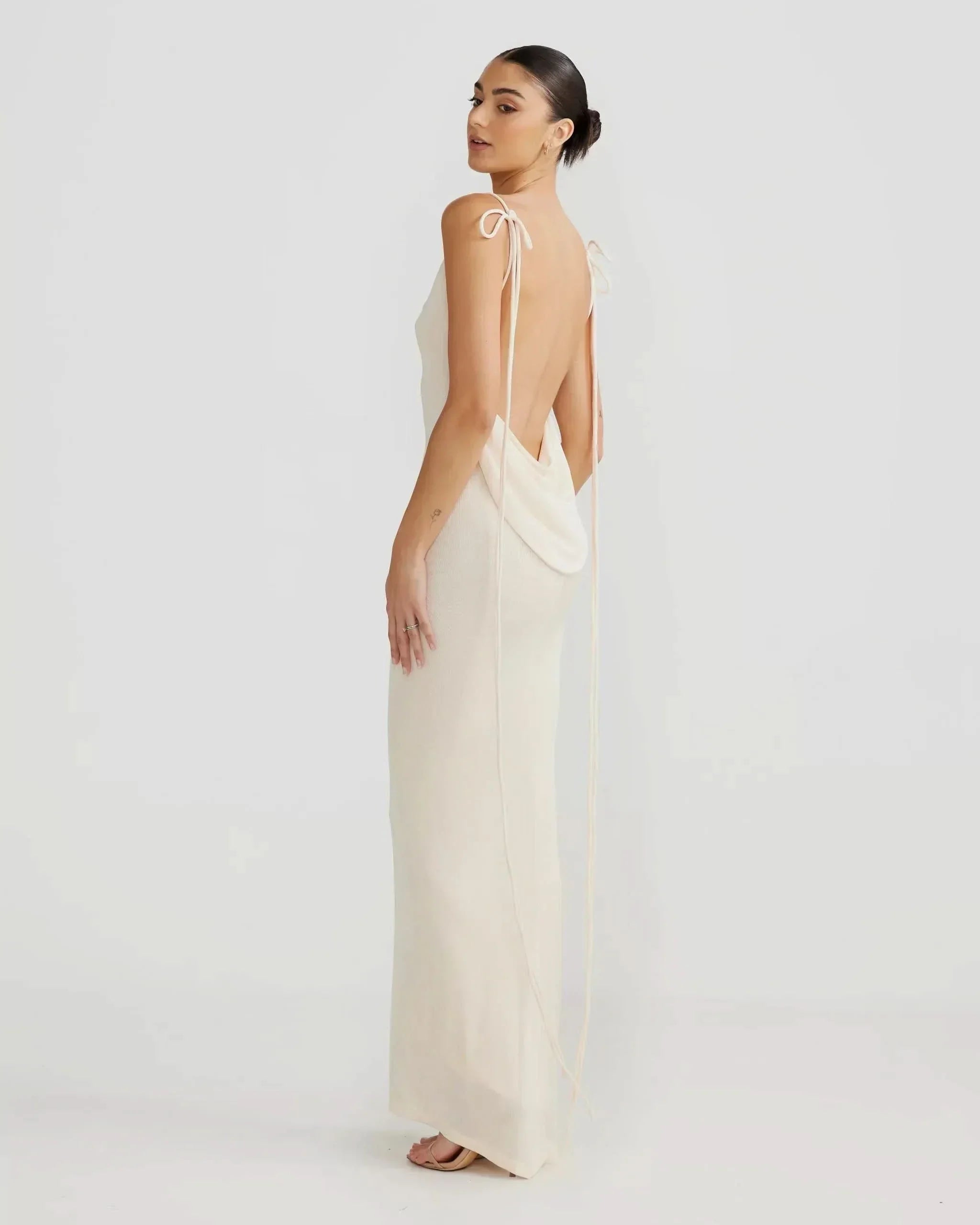 Side profile of a model wearing off-white backless cowl neck maxi dress with long tie straps for women