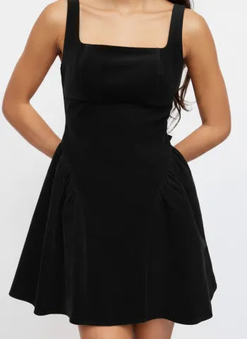 Torso view of a woman in a black Lillie Bow Mini Dress, showing the fitted bodice and flared skirt with pleats.