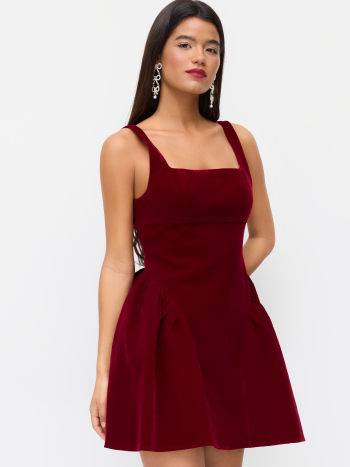 Side profile of a model in a Lillie Bow Mini Dress crafted from red velvet, featuring a square neckline and a full, pleated skirt.