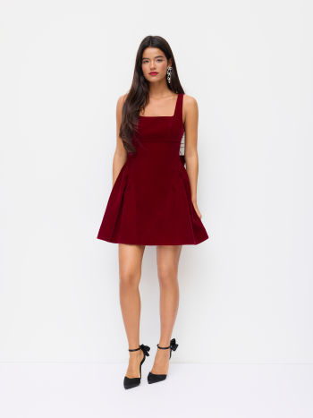 Full-length front view of a model wearing a Lillie Bow Mini Dress in red velvet, paired with black heels with bow accents.