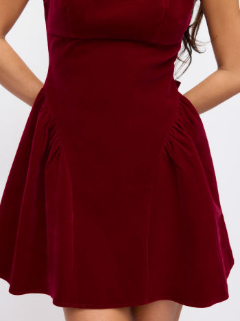 Close-up detail of the pleated skirt and waistline of the Lillie Bow Mini Dress in red velvet, showing the fabric texture.