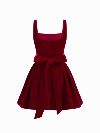 Back view of a Lillie Bow Mini Dress in deep red velvet, featuring a large bow tie detail at the waist and a full, pleated skirt.