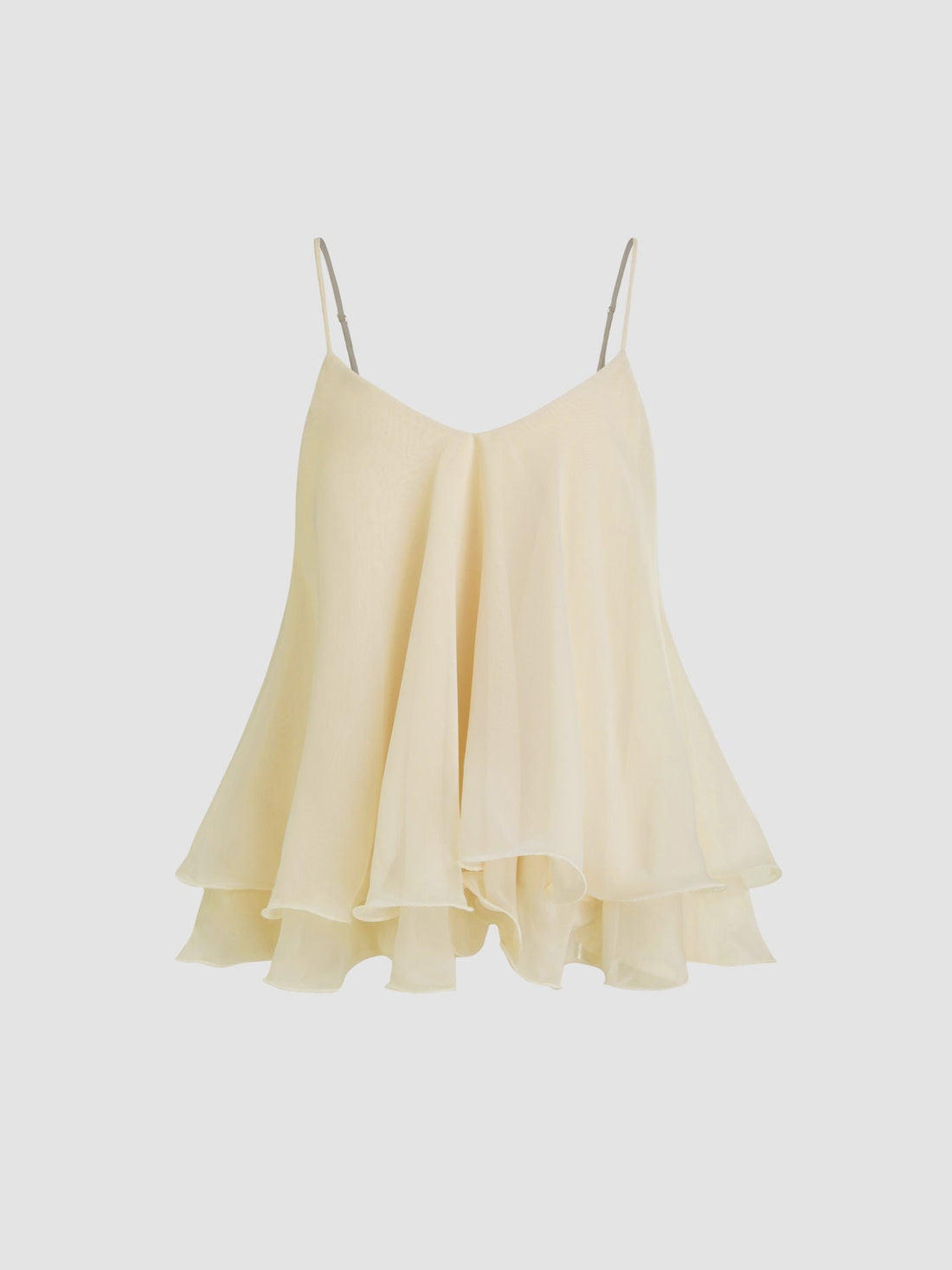 Model wearing a light pink Lily Ruffle Cami Top with delicate ruffles and thin straps, paired with an olive mini skirt and gold jewelry, set against a floral backdrop.