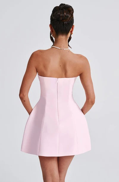 Back view of a woman in a light pink strapless Lola Bubble Mini Dress, showcasing the elegant silhouette and pearl necklace.