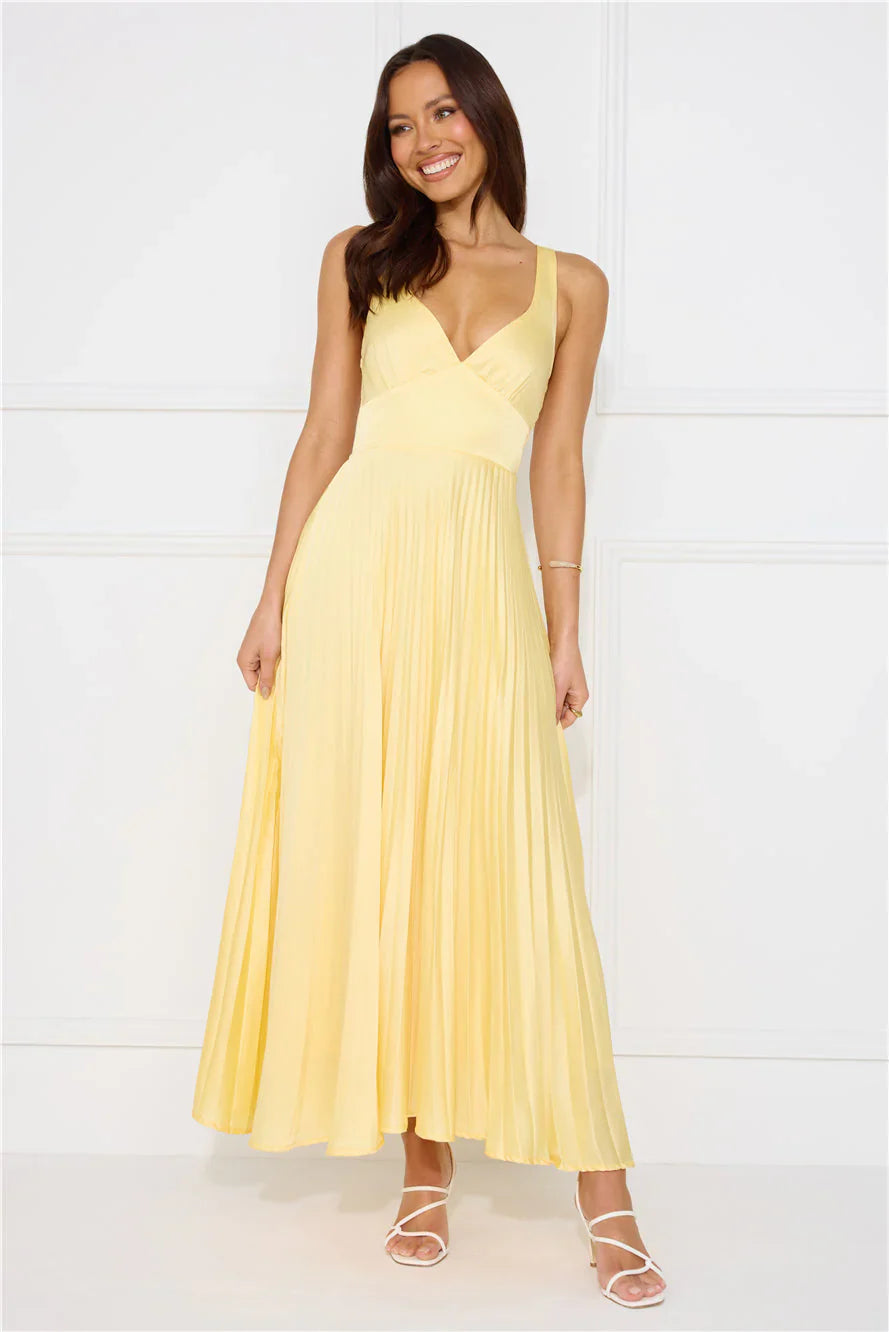 Smiling woman in a light yellow pleated maxi dress with a V-neckline, holding the skirt, for women