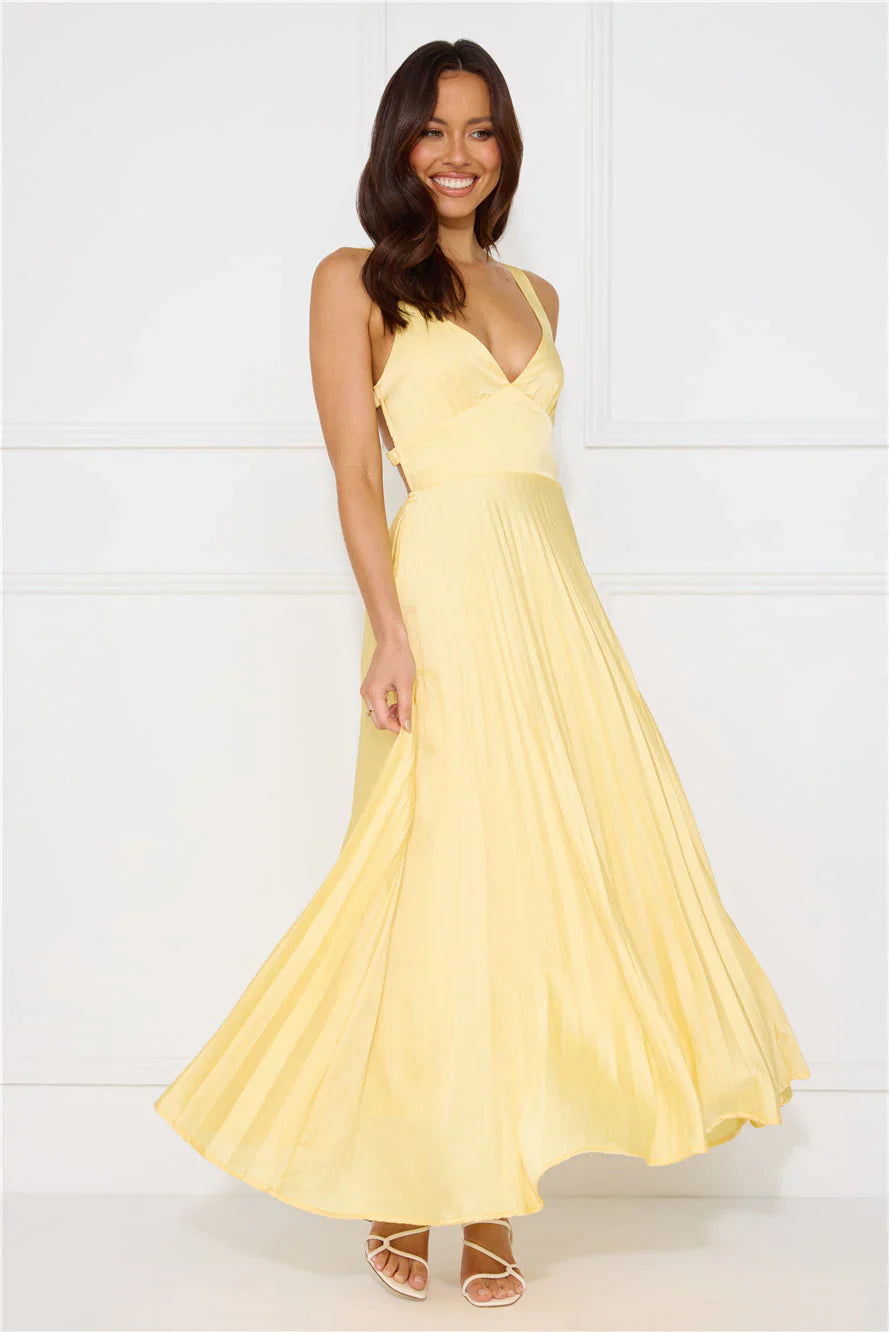 Woman in a light yellow pleated maxi dress with a flowing skirt and V-neck, looking to the side for women
