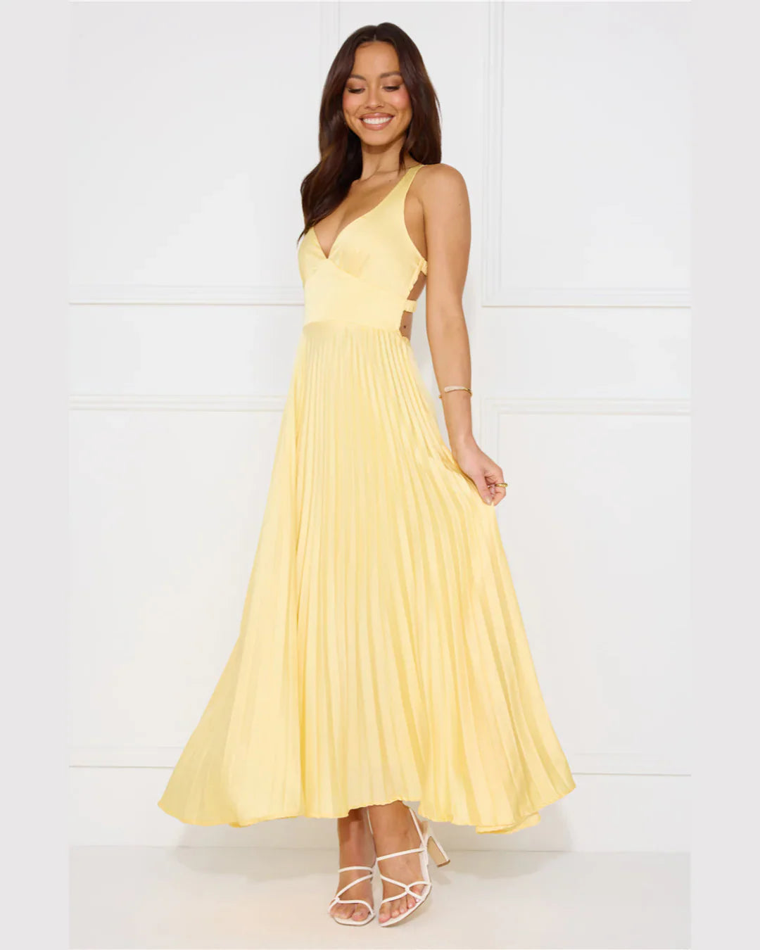 Smiling woman in a light yellow pleated maxi dress with a V-neckline, holding the skirt, for women