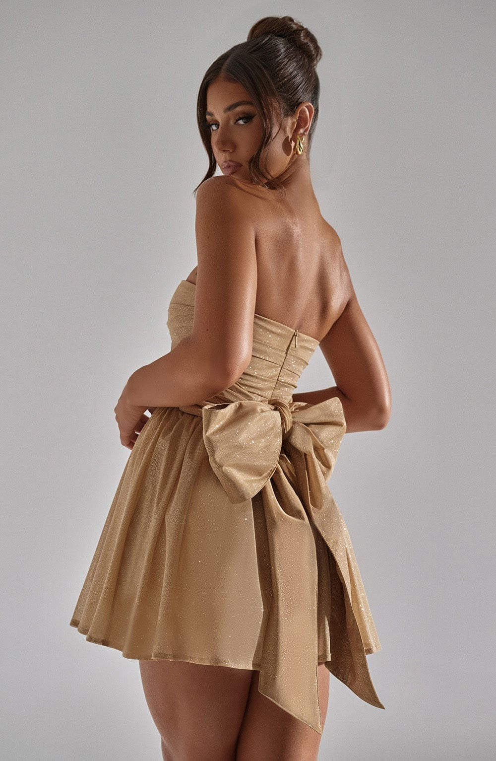 Back view of the champagne gold glitter mini dress, highlighting the large, structured bow detail at the waist.