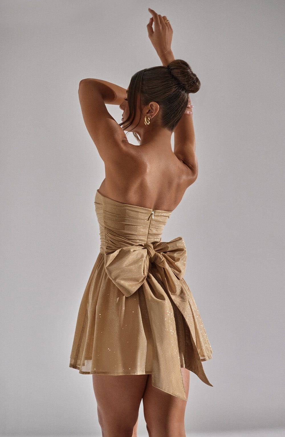 Rear view of the champagne gold glitter mini dress, showcasing the strapless back and the prominent bow detail.