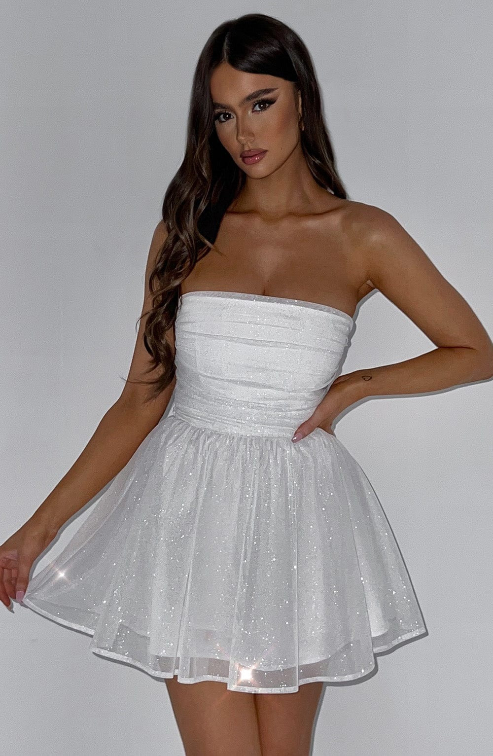 Front view of a white glitter mini dress, featuring a strapless, ruched top and a full, sparkling skirt.