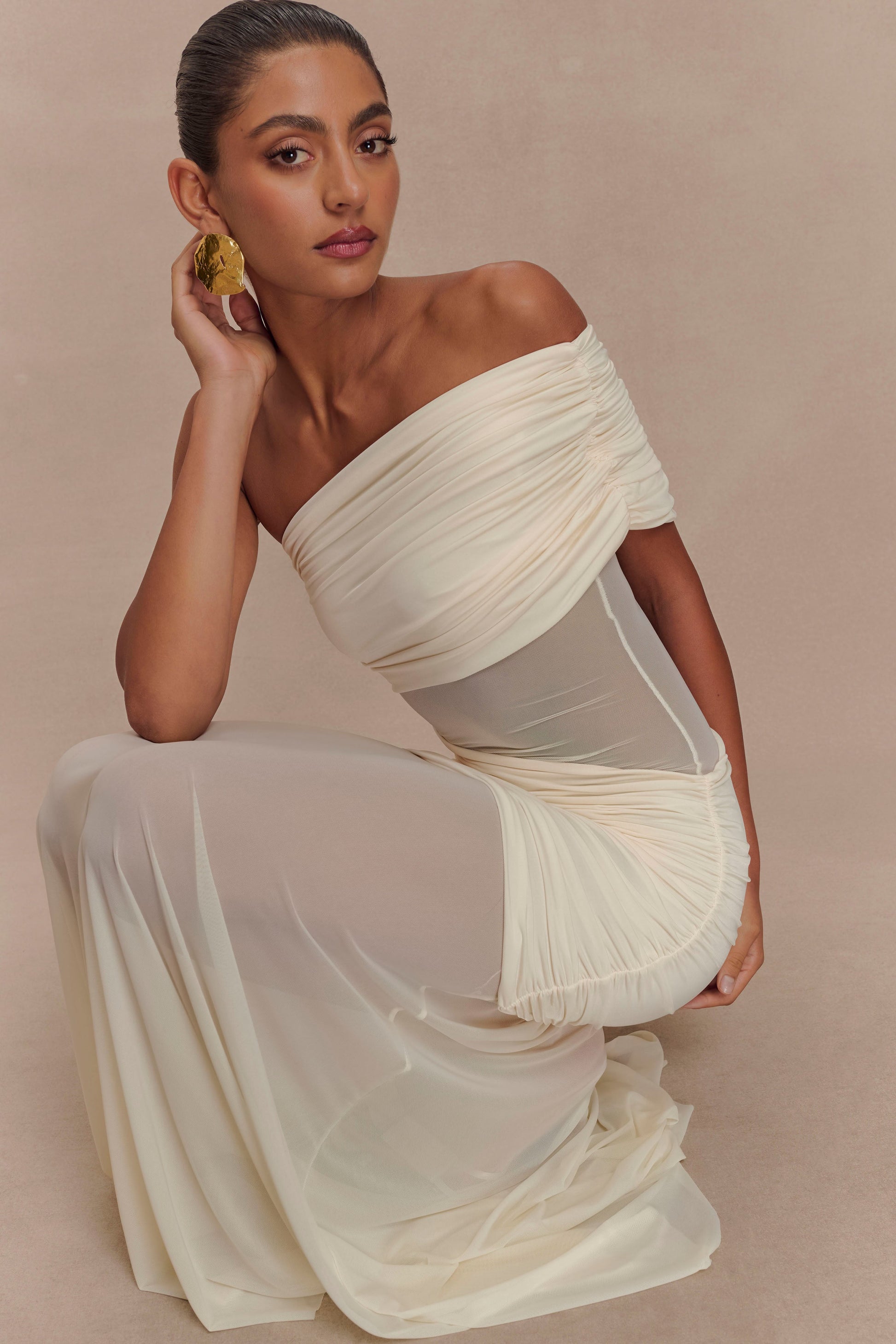 Model crouching in the ivory Luella cutout maxi dress, showcasing the ruched details and sheer flowing skirt.