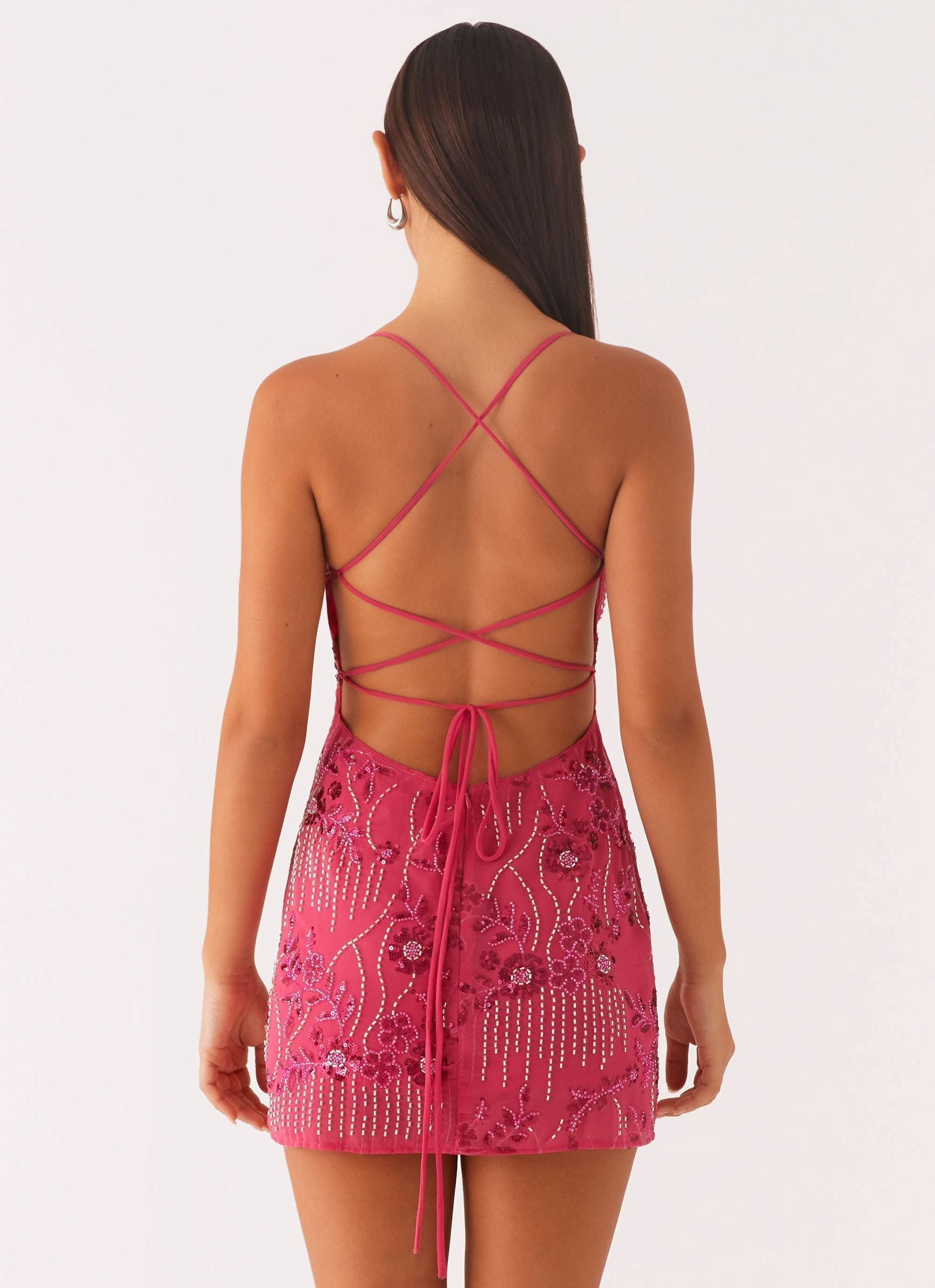 Back view of a pink sequin mini dress with cross-back spaghetti straps and floral beading detail.
