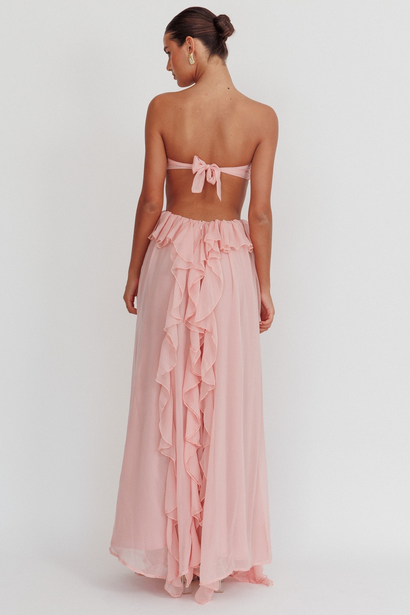 Back view of the light pink Madeleine Rosette Maxi Dress, showing the tie-back bodice and cascading ruffles down the skirt.