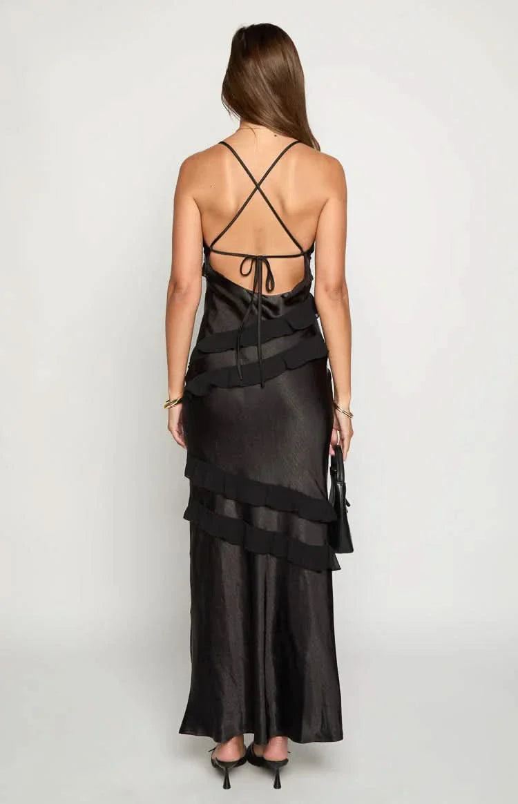 Back view of a black Madeline ruffle maxi dress, featuring criss-cross back straps and horizontal tiered ruffles, with a woman holding a black handbag.