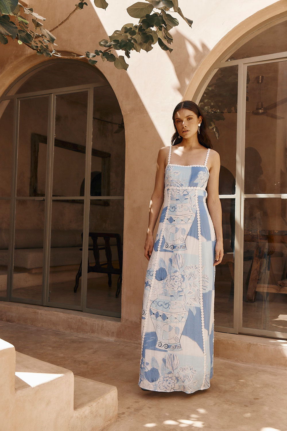 Woman in a blue and white patchwork maxi dress with a back bow and spaghetti straps, standing gracefully in an arched hallway for women.