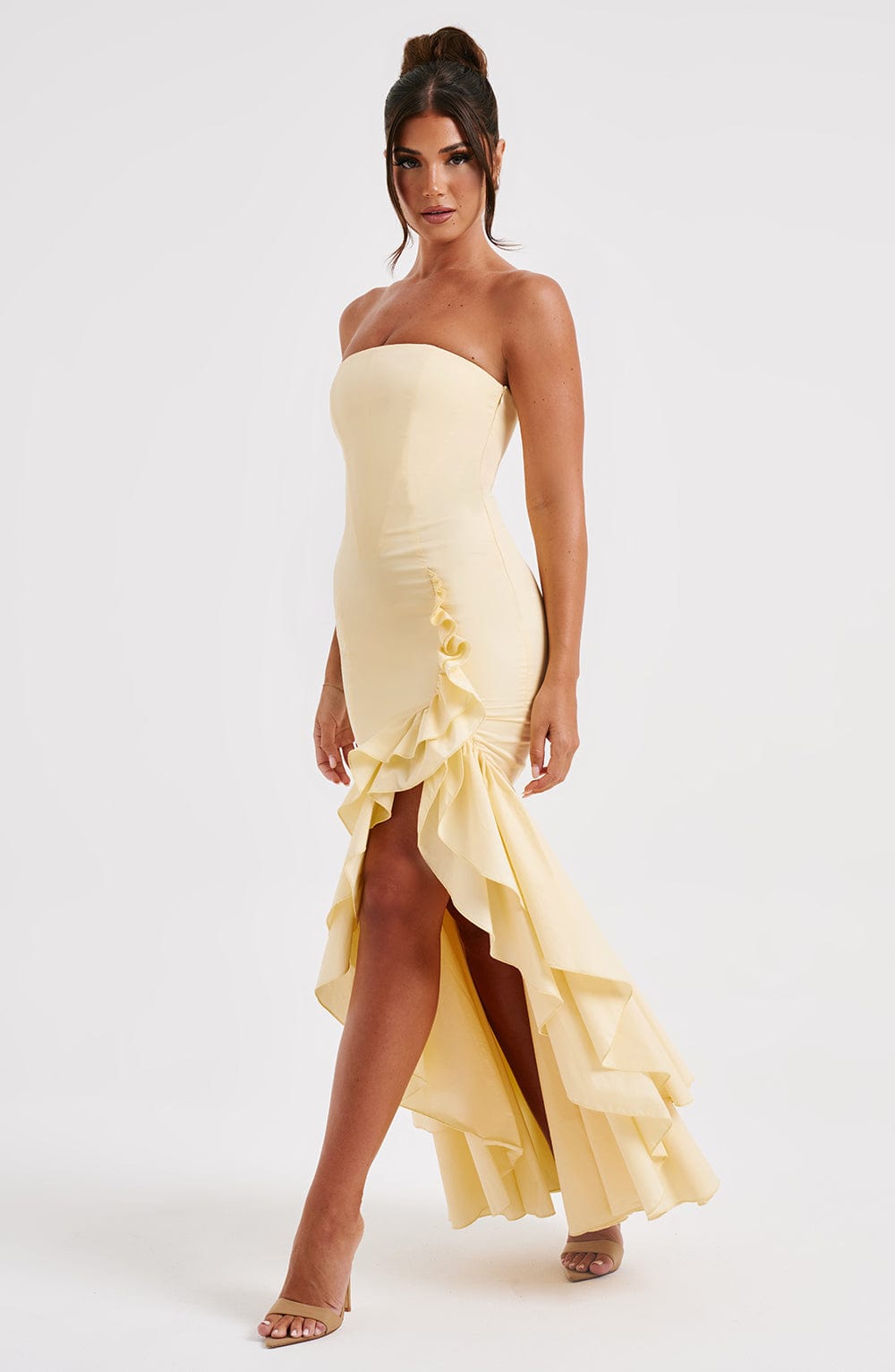 Woman posing in a strapless light yellow Marlowe Ruffle Maxi Dress, featuring a high-low ruffled hem and thigh slit.
