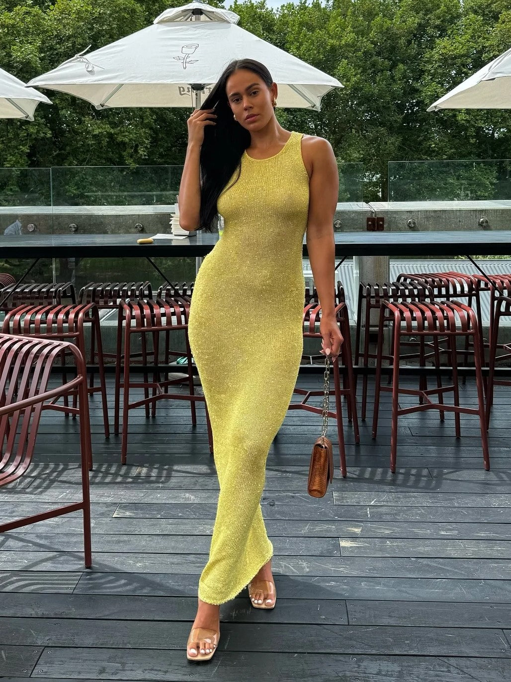Yellow shimmer maxi dress with a scoop neck, worn with clear strap heels and a small brown handbag at an outdoor cafe.