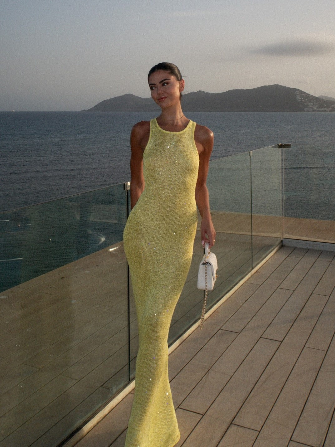 Lime green shimmer maxi dress with a scoop neck and fitted design, paired with a white chain-strap handbag.