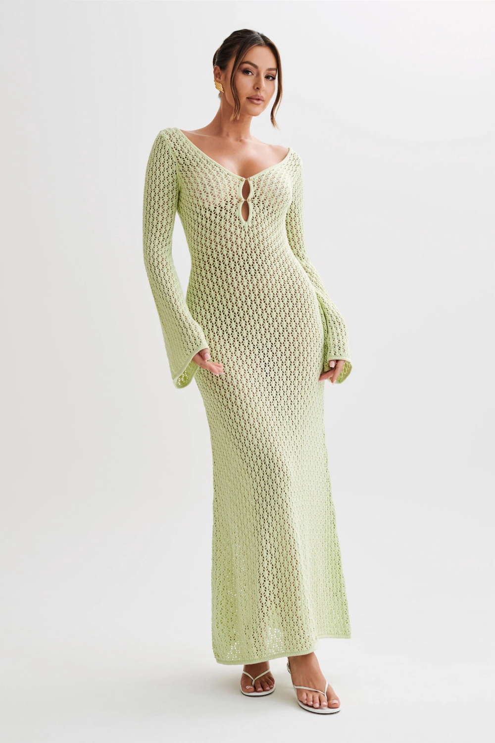 Front view of a light green crochet maxi dress featuring a deep V-neckline, long bell sleeves, and a delicate front tie closure, ideal as a dress suit.