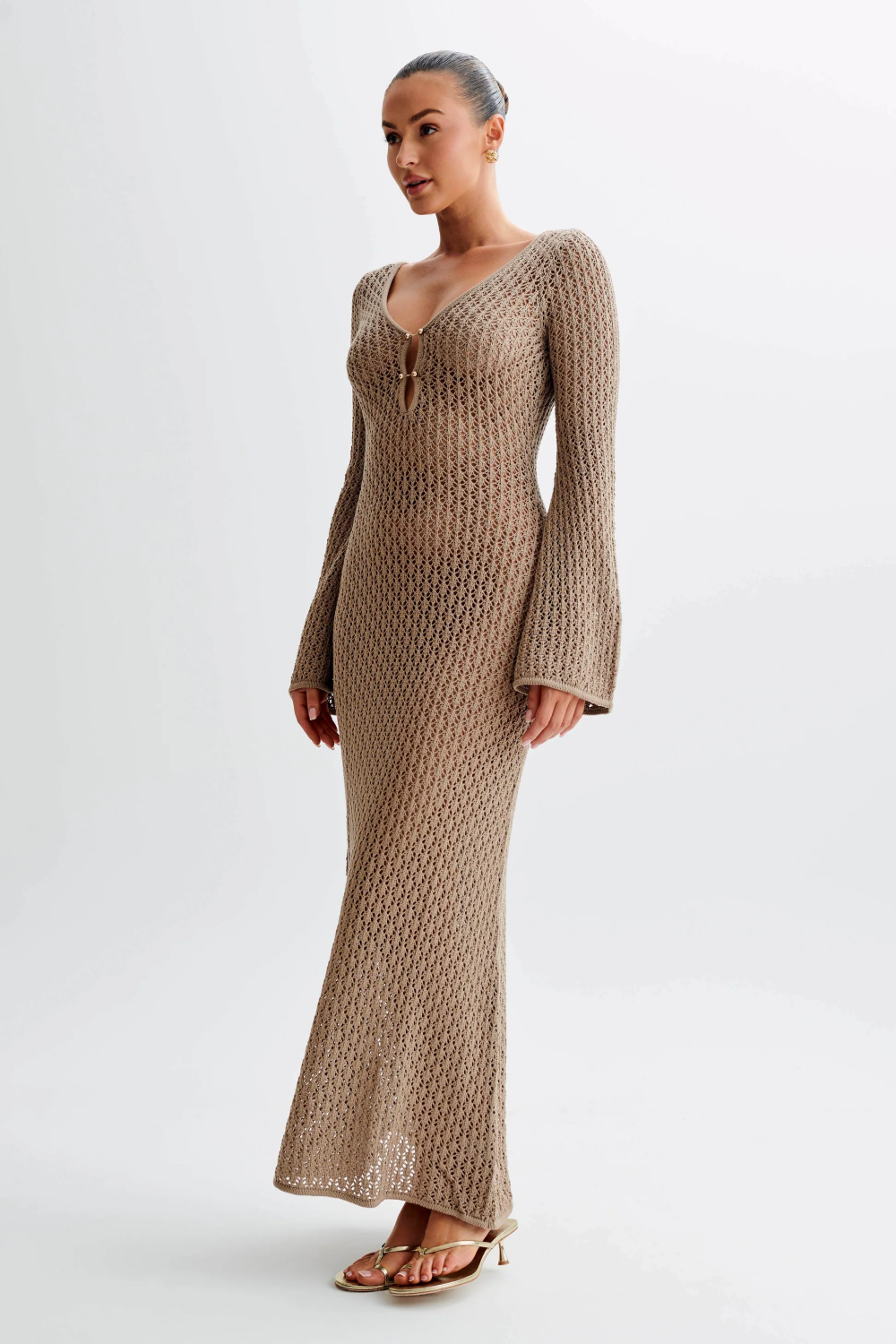 Full-length view of a woman wearing a brown crochet maxi dress with long bell sleeves and a V-neckline.