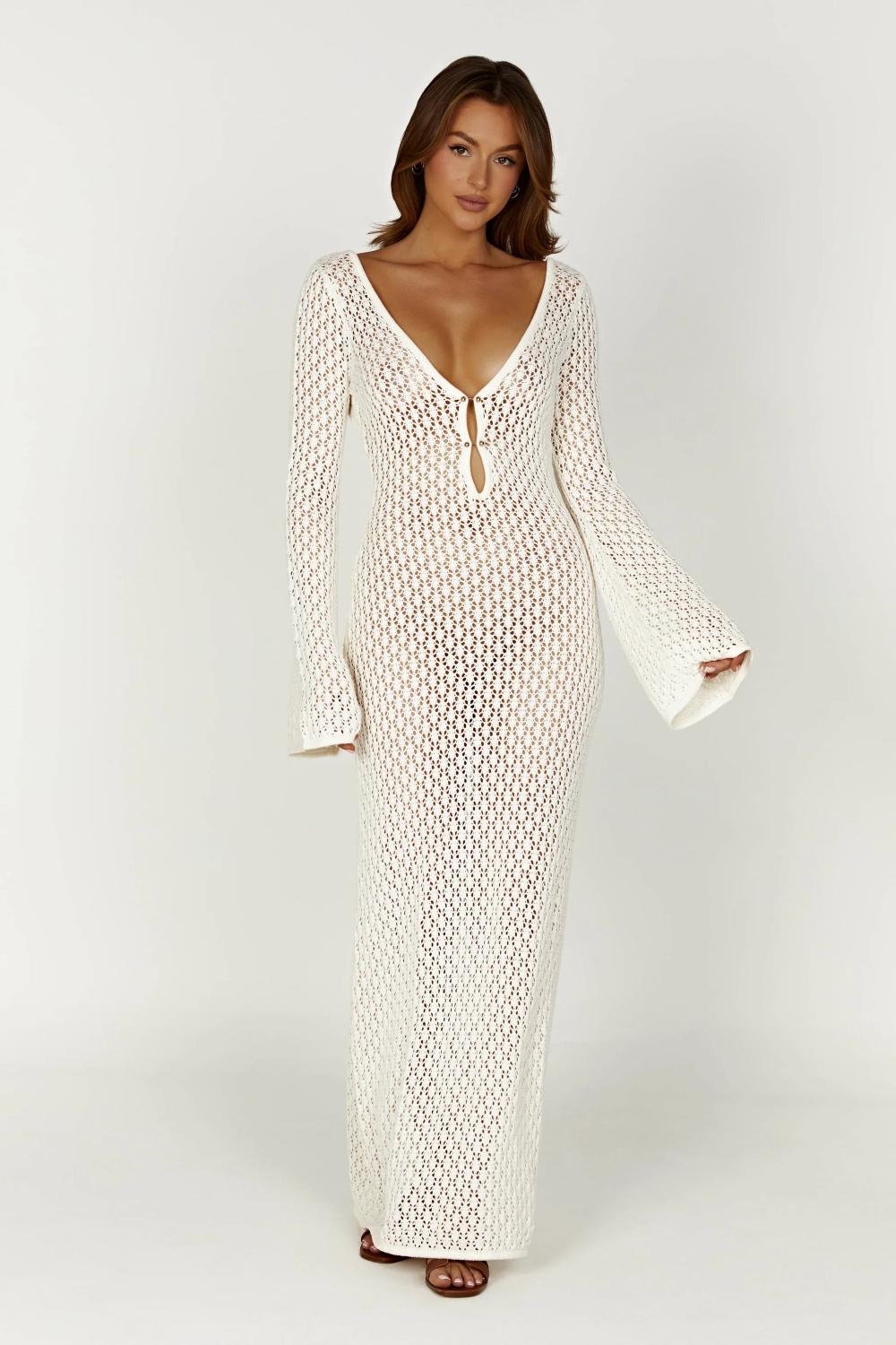 Full-length white crochet maxi dress with long bell sleeves and a deep V-neckline with tie detail.