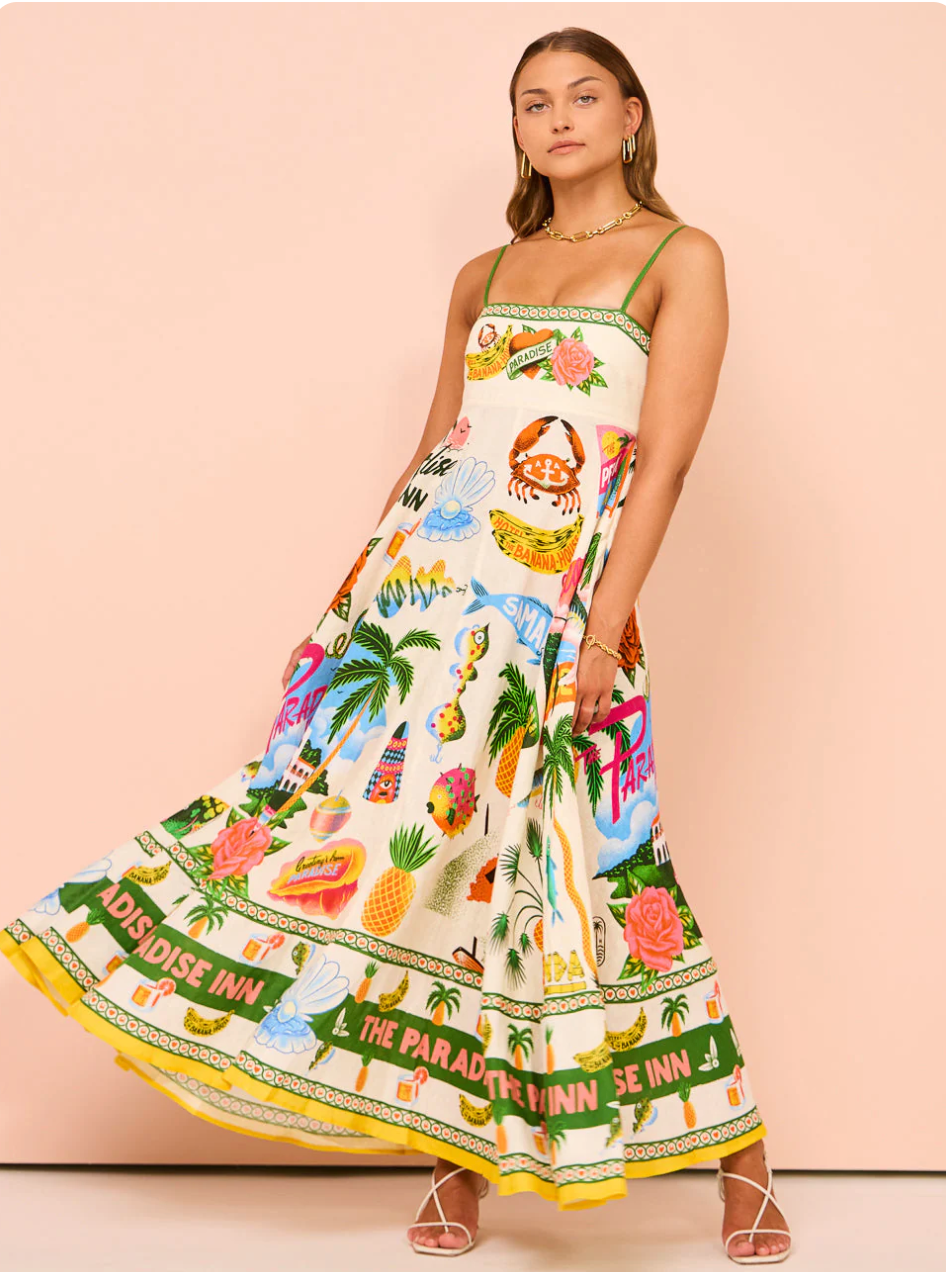 Front view of a flowing white tropical maxi dress with green straps and vibrant resort illustrations, featuring a wide skirt.