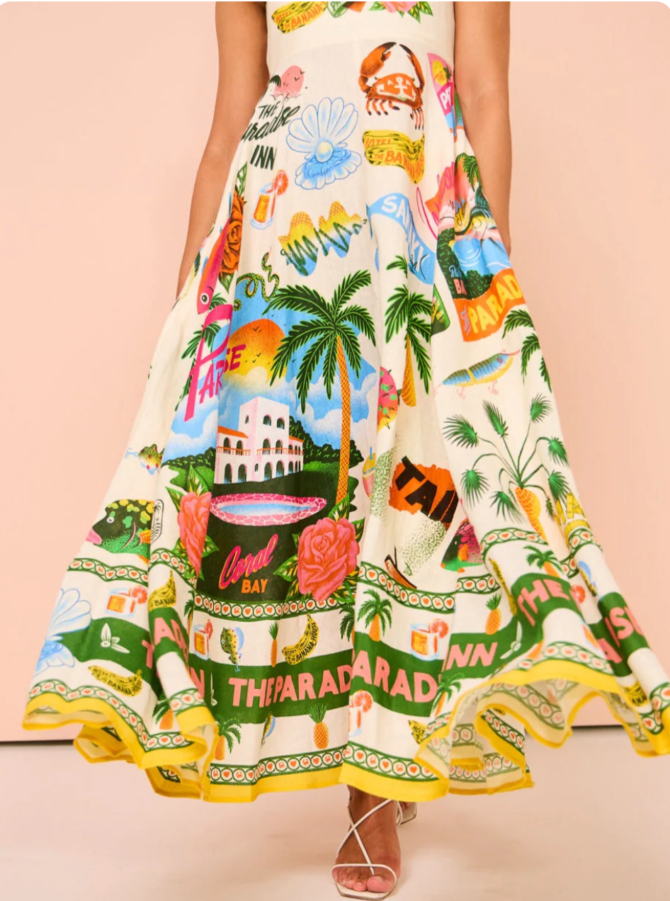 Close-up of the lower half of the white tropical maxi dress, featuring a wide, flowing skirt with vibrant resort and floral patterns.