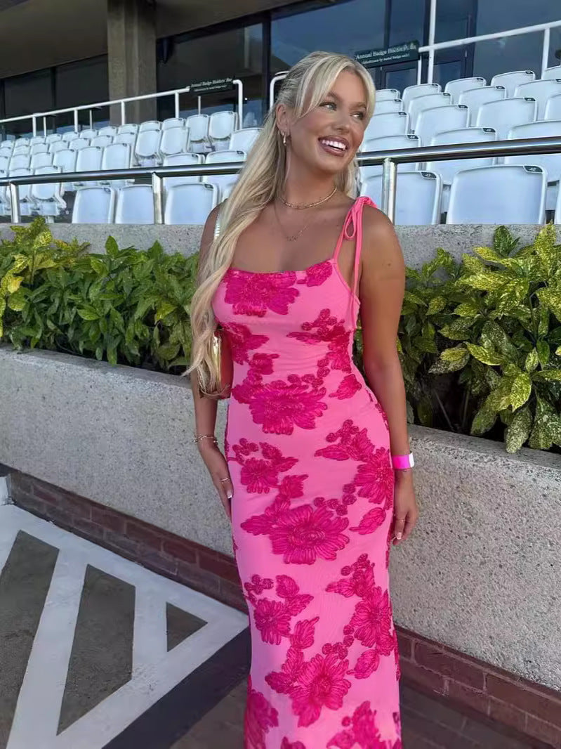 Close-up of a smiling woman in a hot pink floral maxi dress with tied shoulder straps, looking right.