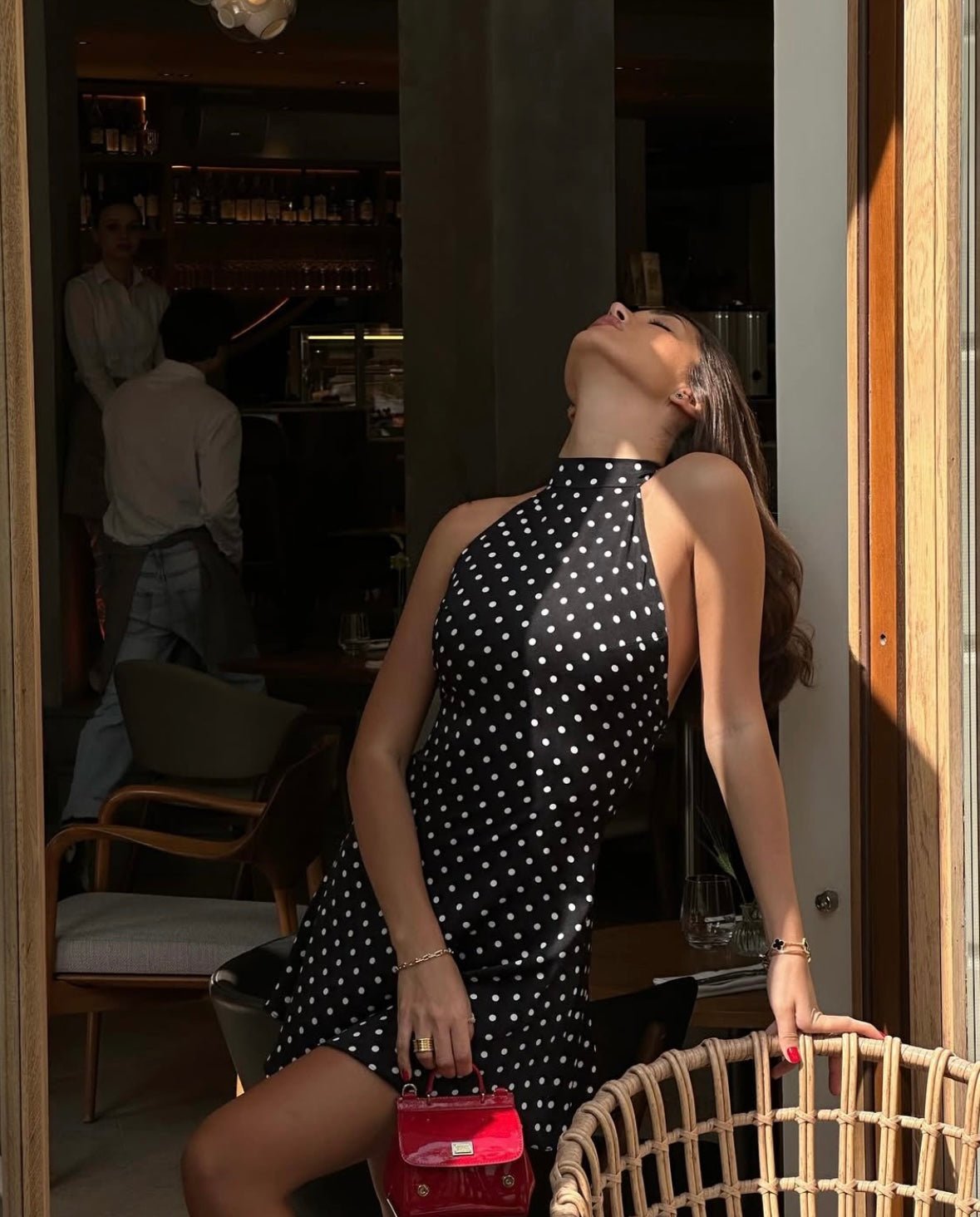 Side profile of a woman wearing a black polka dot mini dress with a halter top and open back.