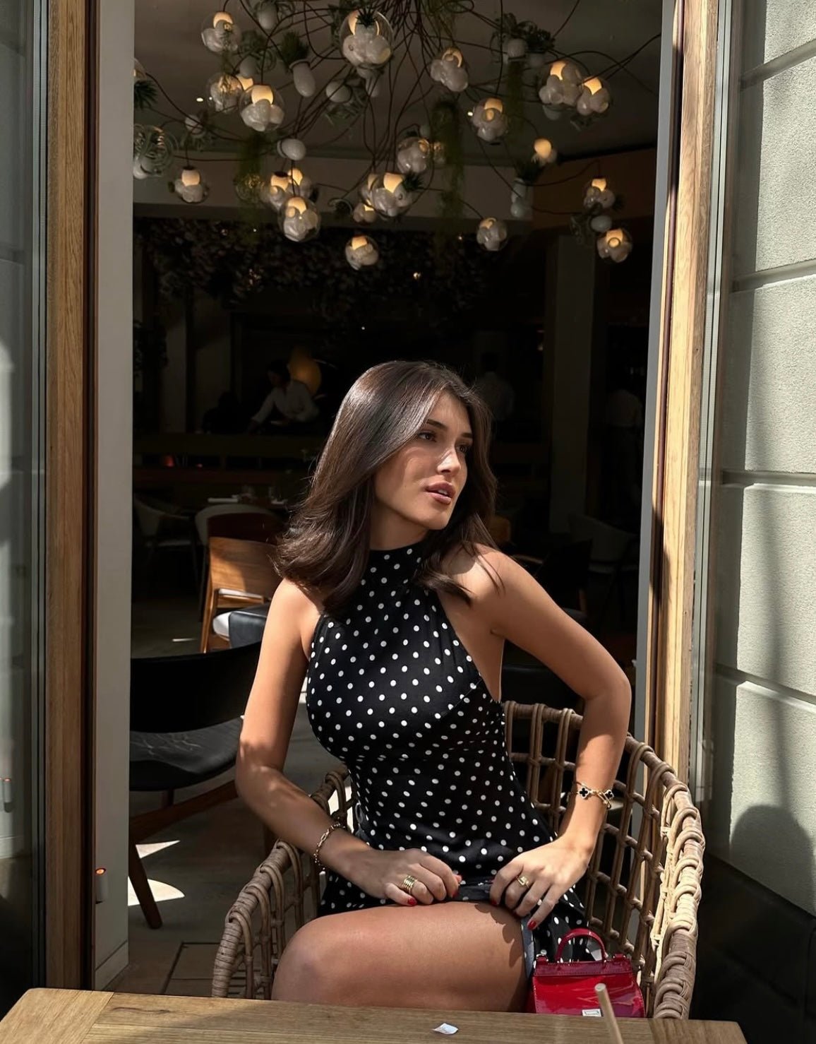 Woman seated in a black polka dot mini dress, featuring a high halter neck and a playful, short hemline.