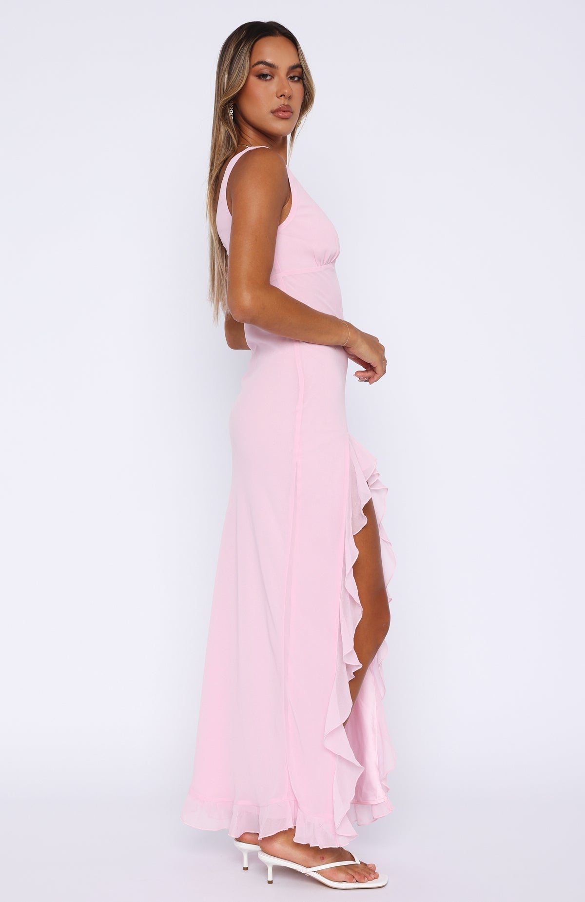 Side profile of a pink ruffle maxi dress, highlighting the flowing ruffles along the high slit and hemline.