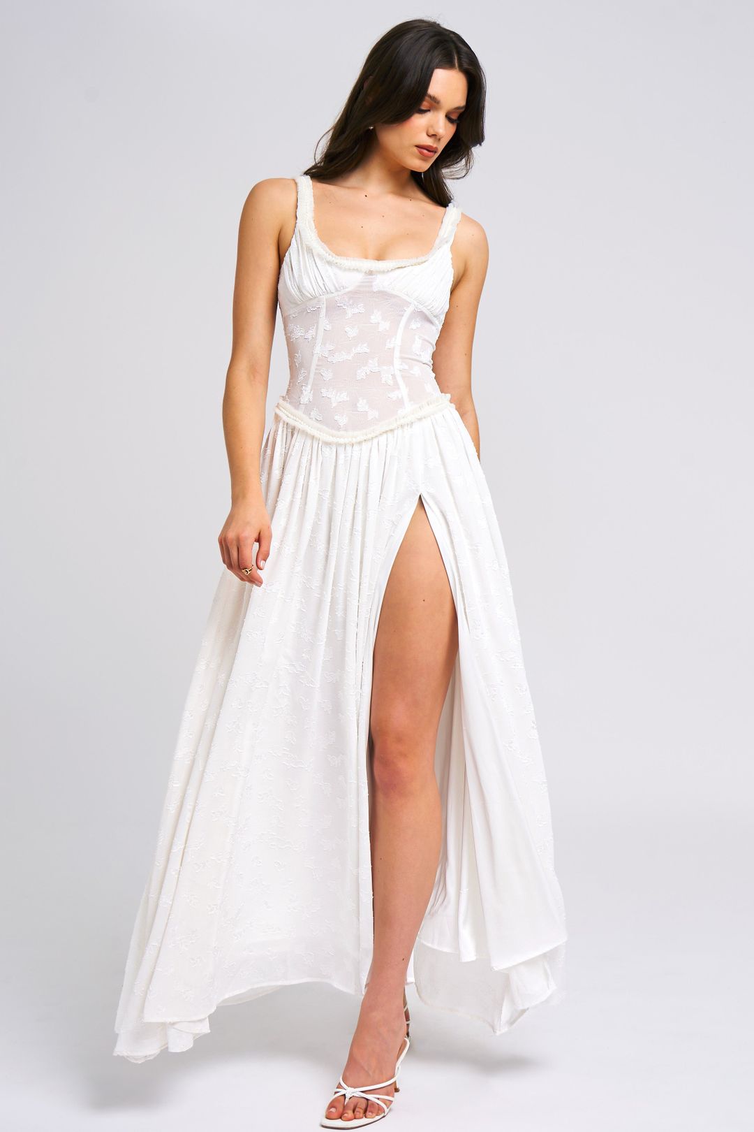 Angled view of the white Nina Corset Maxi Dress, emphasizing the sheer corset top, pearl trim, and dramatic thigh-high slit.