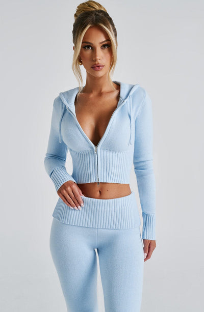 Woman wearing a light blue knitted cropped hoodie with a silver zipper and coordinating ribbed light blue slacks.