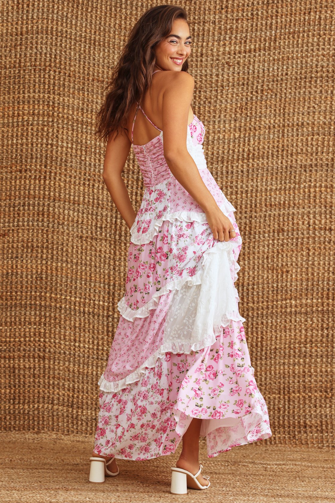 Side view of the pink floral Nola Ruffle Maxi Dress, showcasing the flowing tiered skirt, white lace accents, and white block heel sandals.