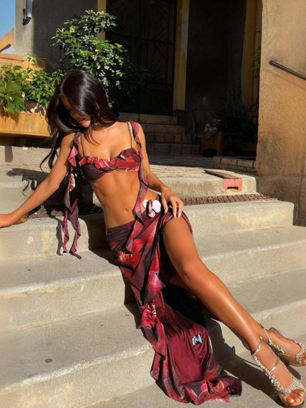 Woman sitting on concrete steps in a red floral tie-front crop top and matching high-slit maxi skirt, with metallic heels.