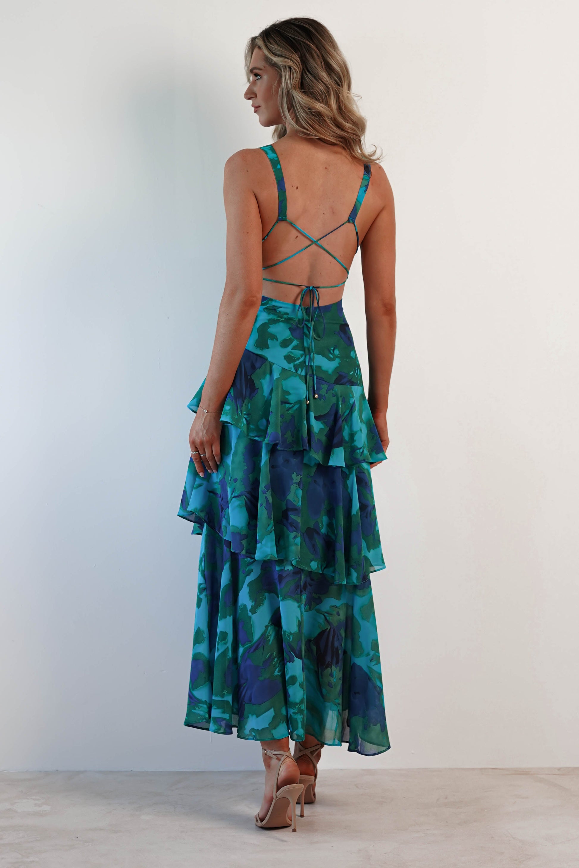 Rear view of a woman wearing a blue and green floral Harriet Ruffle Maxi Dress with tiered ruffles and criss-cross back straps.