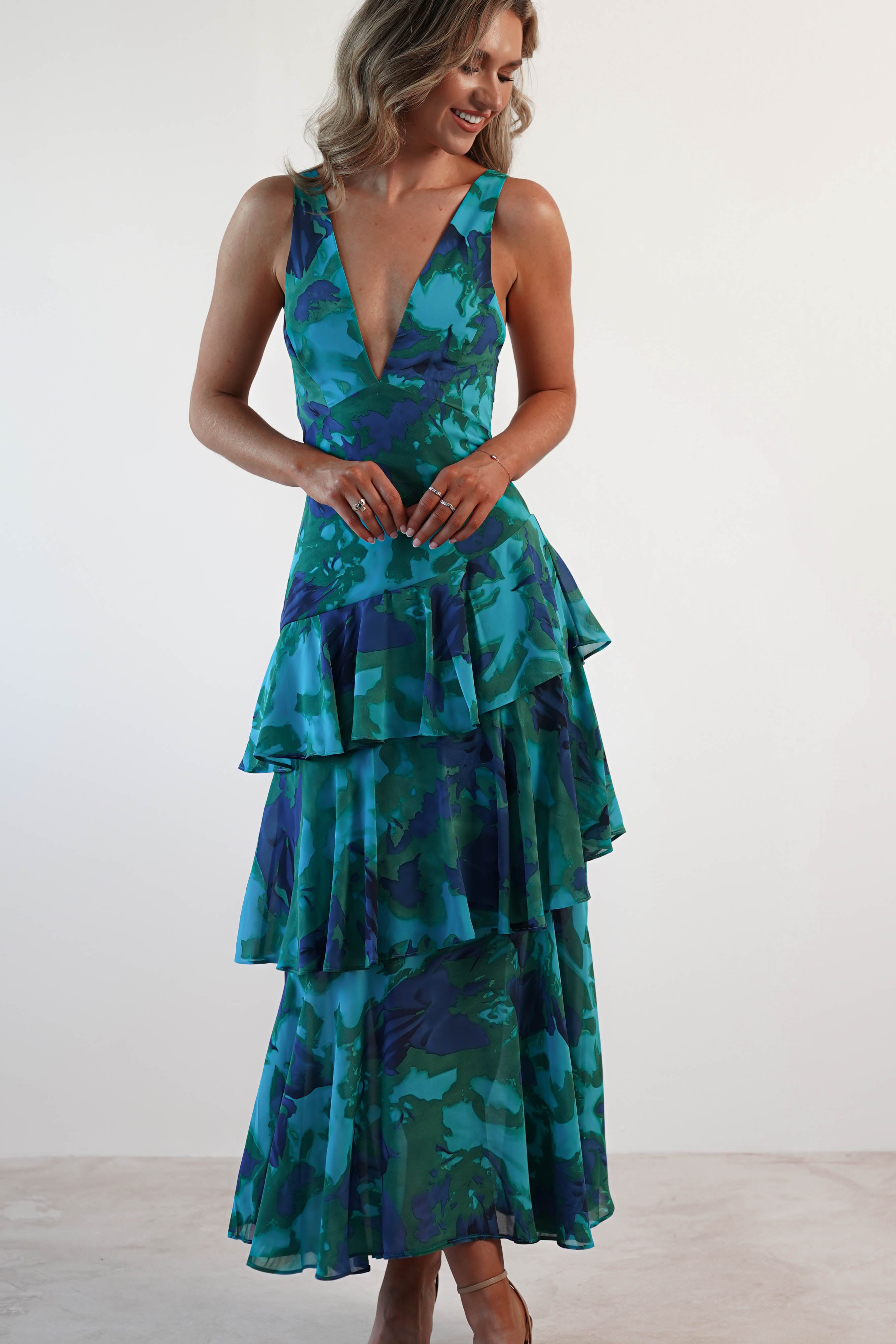 Full-body front view of a woman in a blue and green floral Harriet Ruffle Maxi Dress with a deep V-neck and tiered skirt.