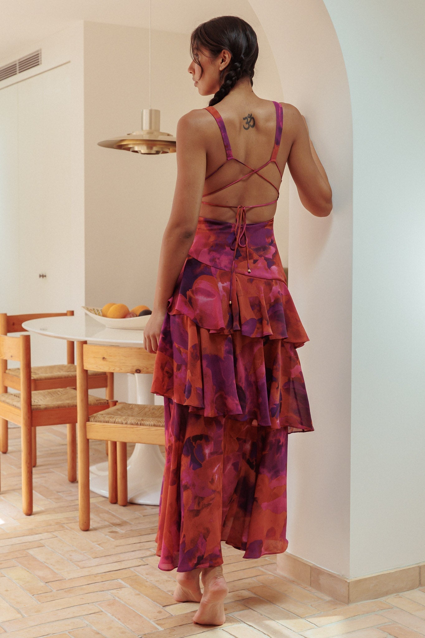 Back view of a woman in a red and purple floral Harriet Ruffle Maxi Dress, showing the criss-cross back detail and tiered skirt.