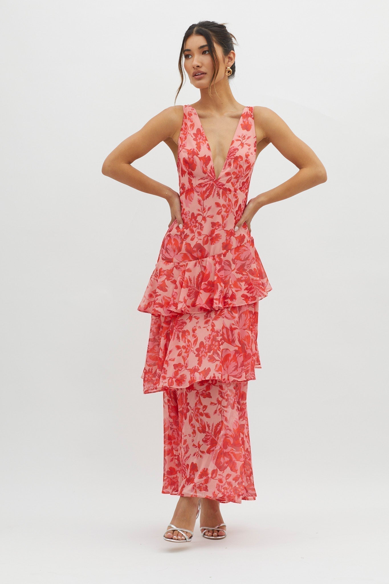 Front view of the pink and red floral Harriet Ruffle Maxi Dress, with hands on hips, highlighting the V-neck and ruffles.