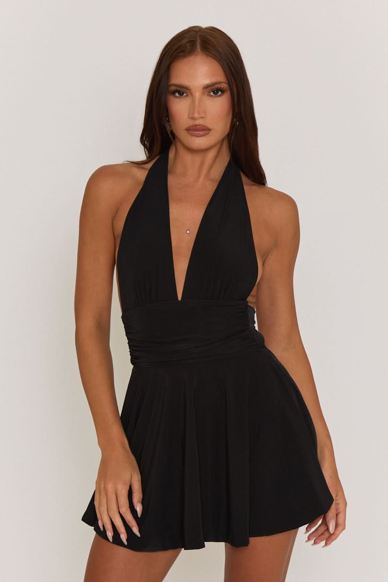 Full-length view of a black halter mini dress with a plunging neckline and flared skirt, worn with clear heels.