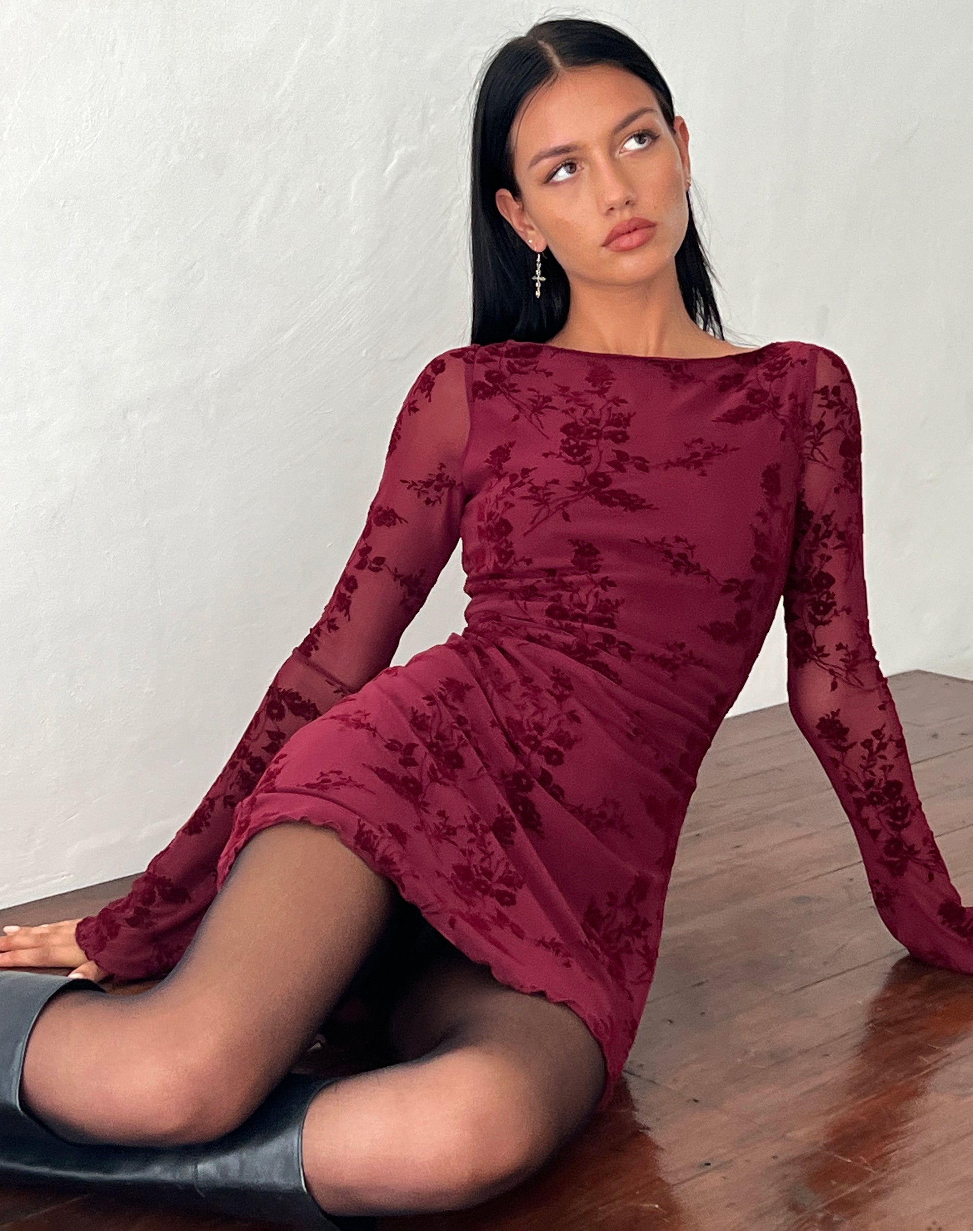 Model sitting on a wooden floor, wearing the dark red Rosalie Scalloped Mini Dress, showing the full length and long sleeves.