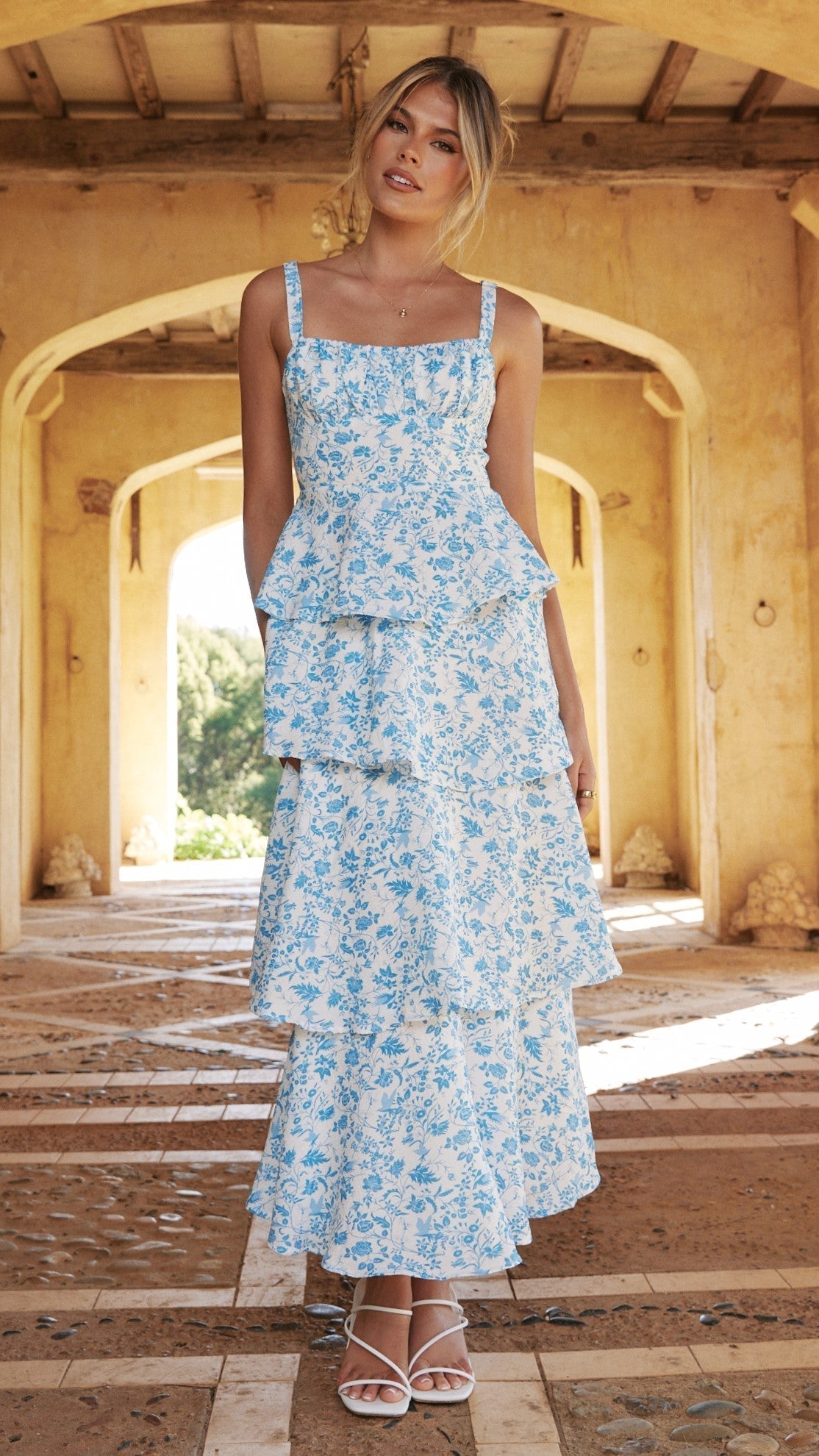 Front view of the blue floral print maxi dress, showcasing the tiered skirt and square neckline, worn with white block heels.
