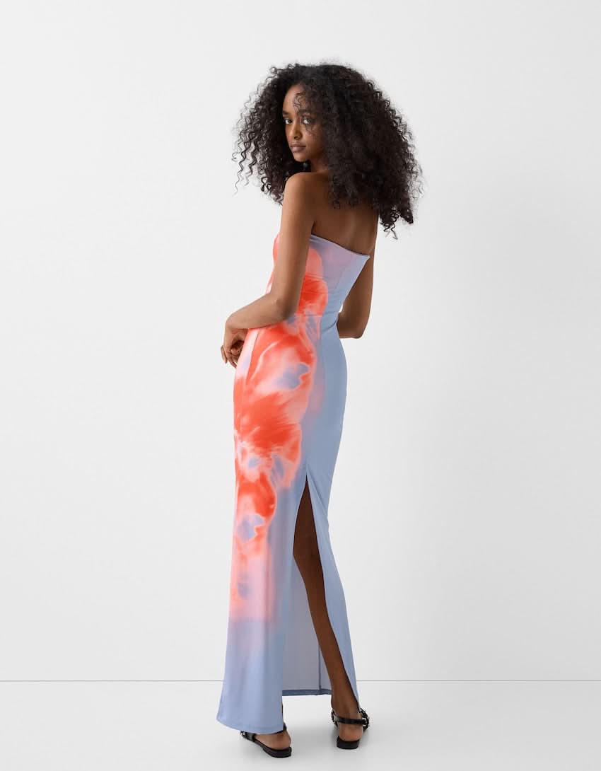 Rear view of women's blue strapless maxi dress with side slit and blurred orange floral print.