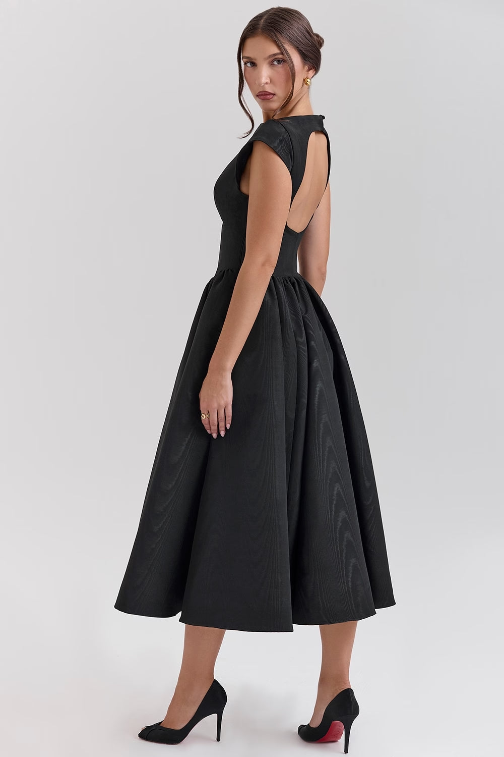 Side profile of the black Sara open-back midi dress, emphasizing the voluminous skirt and sophisticated cut.
