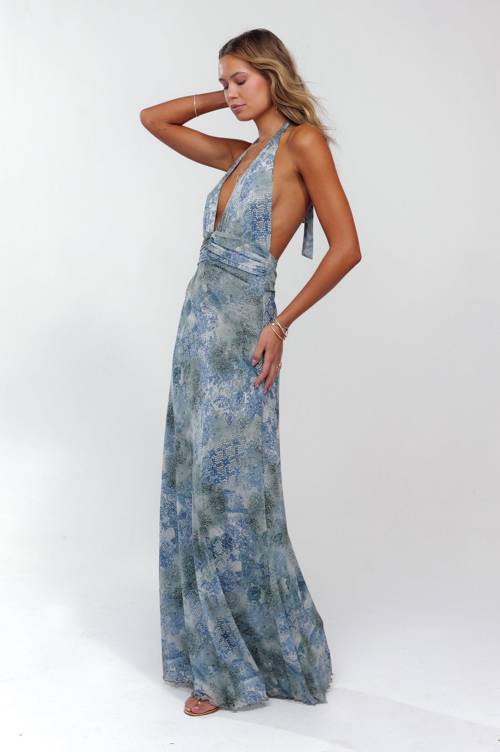 Side view of blue patterned plunge maxi dress, halter neckline, open back, and flowing skirt.