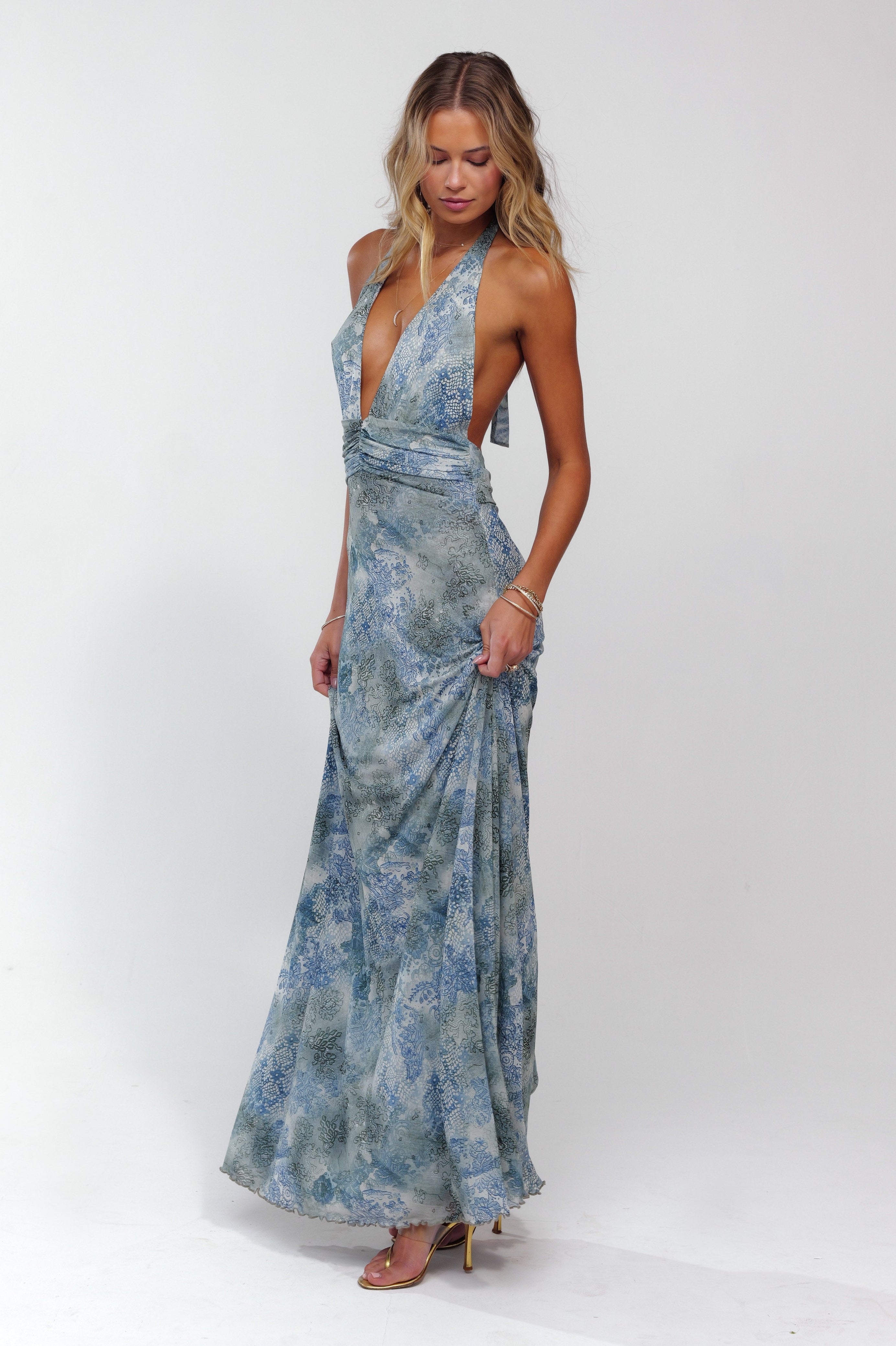 Blue patterned plunge maxi dress with halter top and ruched bodice, flowing skirt, gold heels.