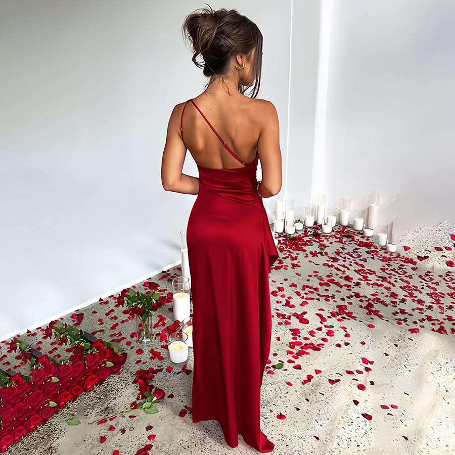 Rear view of a red Sienna Draped Maxi Dress with a single strap, flowing skirt, and romantic rose petal setting.